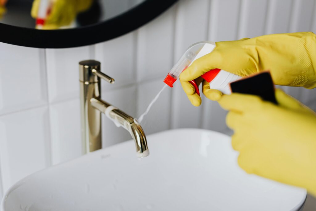 pexels photo 4239130 4239130 From above anonymous housekeeper in yellow rubber gloves spraying cleaner to chrome water faucet in bathroom